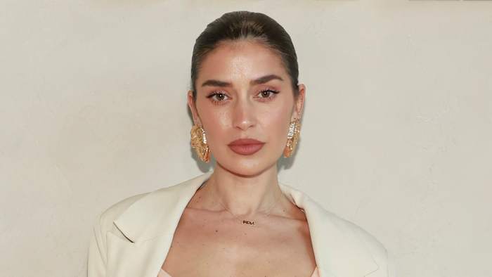 Nicole Williams English poses in a cream-colored corset top, a matching blazer and oversized gold earrings.